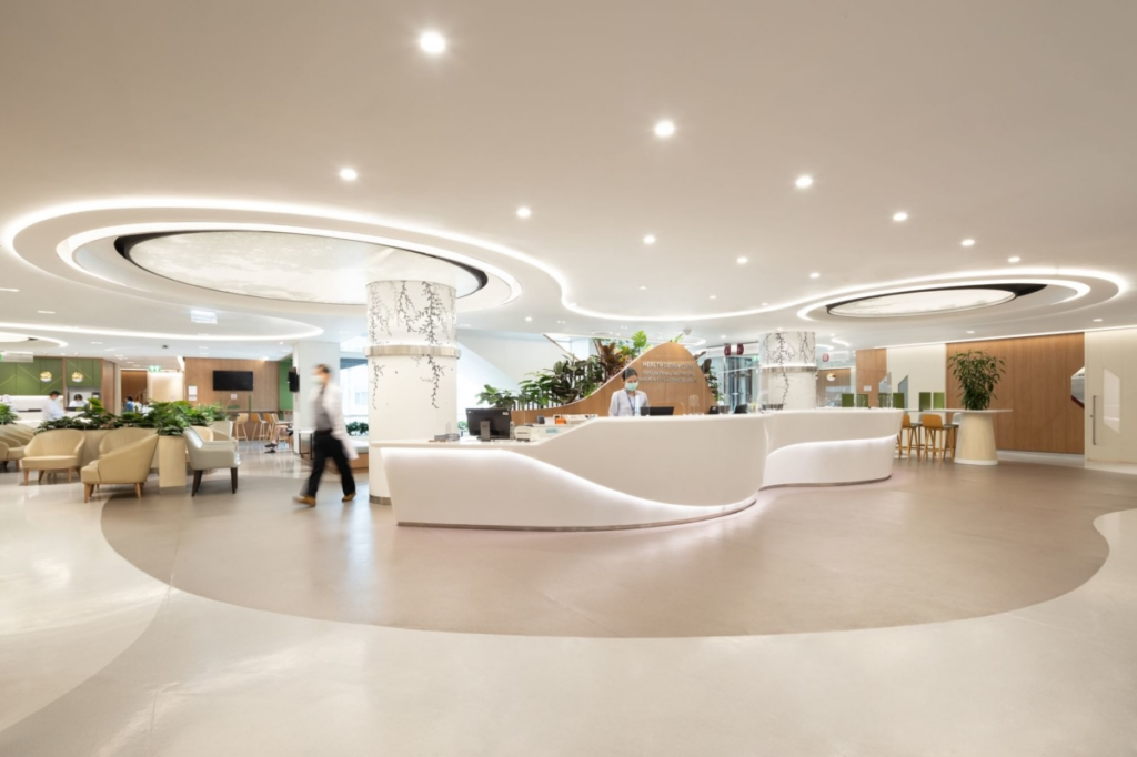 A spacious, contemporary hospital reception area with a curved white front desk, comfortable lounge seating, warm lighting, and modern architectural design. Staff members assist patients in a bright, welcoming environment that emphasizes comfort, efficiency, and high-quality healthcare.