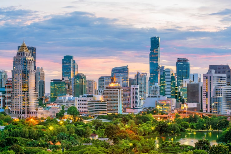 The Bangkok city skyline at dusk with glowing skyscrapers, lush green parkland, and a dramatic pink and purple sky, representing Thailand's position as the world's second-leading medical tourism destination in 2026.
